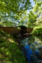 Old renovated retro bridge with green metal railings over small river in small colorful park