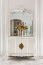 Vintage mirror and flower bouquet on wooden cupboard. Old restored furniture in classic bright interior with white wall Royalty Free Stock Photo