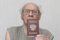 Old retired man not combed in gray shirt is passport in his hand.