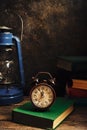 Old retro alarm clock in rustic interior with books and kerosene lamp Royalty Free Stock Photo