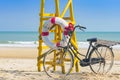 Old retro black bicycle with flowers bouquet beside Life ring for life safety on yellow lifeguard stand station or lifeguard chair Royalty Free Stock Photo