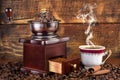 Retro coffee mill and cup with black coffee smoking on wooden background