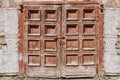 An old retro shabby wooden painted brown double door with a lock and a fragment of an old plastered wall with bare bricks Royalty Free Stock Photo