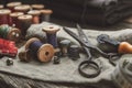 Old retro tailoring scissors, measuring tape, thimble, wooden spools of thread, cutting knife, pin cushion and sewing accessories.