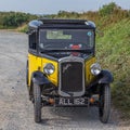 Old retro vintage Austin car with a countryside road and bushes in the background