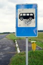 Old road blue bus stop sign damaged by pistole bullets by asphalt road