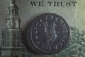 An old Roman coin lies on a 100 dollar bill