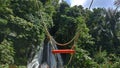 The old rope wooden single swing with orange saddle. Outdoor swing on nature waterfall background with sunlight Royalty Free Stock Photo