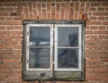 Old rotten double leaf window with mold and moss in brick wall.