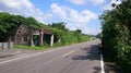 Old ruin covered and overgrown with green plants, empty road, blue sky Royalty Free Stock Photo