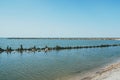 An old ruined pier with wooden logs sticking out of the water from the sea surface. Sandy beach in the foreground Royalty Free Stock Photo