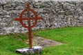 Old, rusted cross marking a grave, with stone wall behind