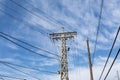 Old rusted industrial metal power line tower alongside a traditional wooden power pole set against a blue sky Royalty Free Stock Photo