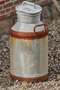 An old rusted metal milk can on the ground from above. An antique dairy canister outside on a pebble covered walkway. A Royalty Free Stock Photo