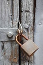 OLD RUSTED PADLOCK ON A WOODEN DOOR WITH FLAKING GREY PAINT