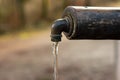 Old rustic drinking water fountain in the forest. Wooden construction, rusty metal pipe and faucet, streaming water. Close up shot Royalty Free Stock Photo