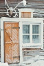 Old rustic house made of timber and covered in snow. The building has a yellow or orange wooden door and a window next to it. Royalty Free Stock Photo