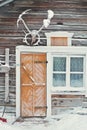 Old rustic house made of timber and covered in snow. The building has a yellow or orange wooden door and a window next to it. Royalty Free Stock Photo