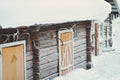 Old rustic house made of timber and covered in snow. The building has yellow or orange wooden doors. Some tools on the side of the Royalty Free Stock Photo