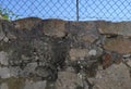 Old, rustic stone wall with wire fence on top and blue sky behind Royalty Free Stock Photo
