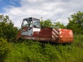 An old rusty abandoned backhoe, a machine for heavy work, overgrown with grass and thorns during a cloudy summer day