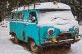 An old rusty ambulance van stands in a snow-covered clearing on a cloudy winter day