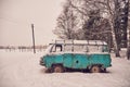 An old rusty ambulance van stands in a snow-covered clearing on a cloudy winter day