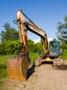 An old rusty backhoe, a heavy-duty machine, against a green grove during a sunny summer day