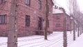 Old rusty barbed wire fence of Auschwitz Birkenau concentration and extermination camp. Brick barracks in falling snow Royalty Free Stock Photo