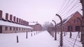 Old rusty barbed wire fences and concentration camp buildings. Brick barracks, lonely man in falling snow Royalty Free Stock Photo