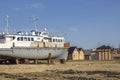 Old rusty battered ship on supports on the shore against the background of wooden houses