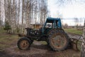 An old rusty blue tractor among the trees in the open air on a driverless farm. Royalty Free Stock Photo