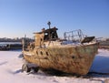 Old rusty boat moored to the shore in the winter froze on the river