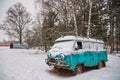 An old rusty ambulance van stands in a snow-covered clearing on a cloudy winter day