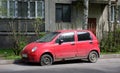 An old rusty broken red car is parked on the street