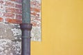 Old rusty copper and cast iron downpipe against a brick and yellow plaster wall Royalty Free Stock Photo