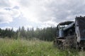 An old rusty crawler tractor, abandoned in a field, against the background of a pine forest in Siberia. decline and Royalty Free Stock Photo