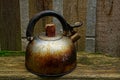 Old rusty and dirty teapot is standing by the wooden fence