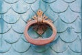 Old rusty door knocker on a teal painted door with a fish scales pattern