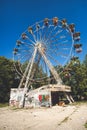 An old rusty ferris wheel in a closed abandoned USSR theme amusement park. Sad post apocalypse atmosphere in a sunny summer day