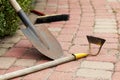 Old rusty garden tools laying on stone paved walkway with gray and pink pavements. Used hoe, shovel and brush, the soil spots on t