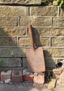 Old rusty gardening spade propped up against a garden wall