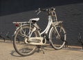 Old rusty grunge vintage white bike in bicycle rack in front of a black brick wall. Royalty Free Stock Photo