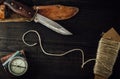 Old rusty hunting bushcraft knife, military compass and a linen rope on the wooden table.