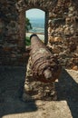 Old rusty iron cannon aiming through window in stone wall