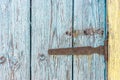 Old rusty iron hinge with nails on wooden door with cracked peeling blue and yellow paint close up. Rural background Royalty Free Stock Photo