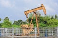 Old rusty isolated oil pump jack extracting crude oil and natural gas from well in green and cloudy oil field Royalty Free Stock Photo