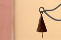 An old rusty metal cone shaped bell is hanging suspended in air outside against a blank tan wall background