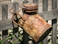 An old rusty milk churn hanging on a wooden fence