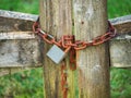 Old rusty padlock on a metal chain on a wooden gate. Green field in the background. Concept security of farmland and private Royalty Free Stock Photo